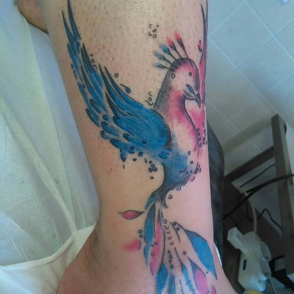 A vibrant phoenix tattoo adorns the arm, showcasing blue wings and pink accents that come to life