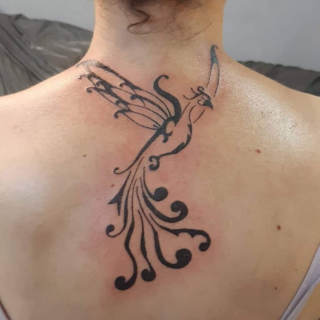 Stylized phoenix tattoo on upper back with ornate tail and wings