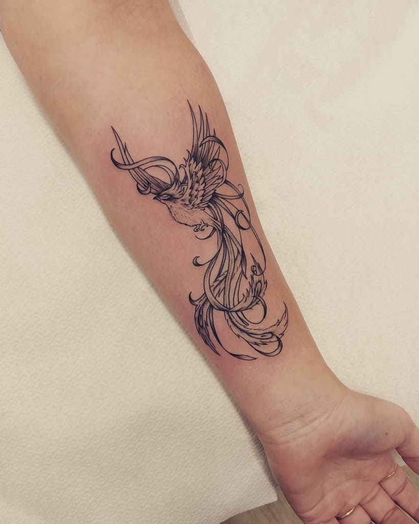 A delicate line-work tattoo of a phoenix on the forearm, featuring intricate swirls and flowing feathers