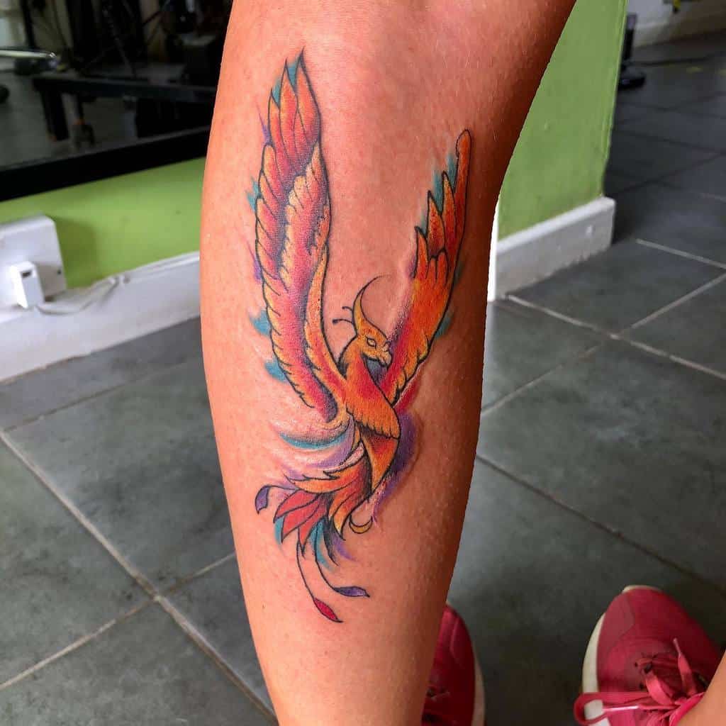 A vibrant phoenix tattoo graces a person's leg, showcasing an array of stunning colors