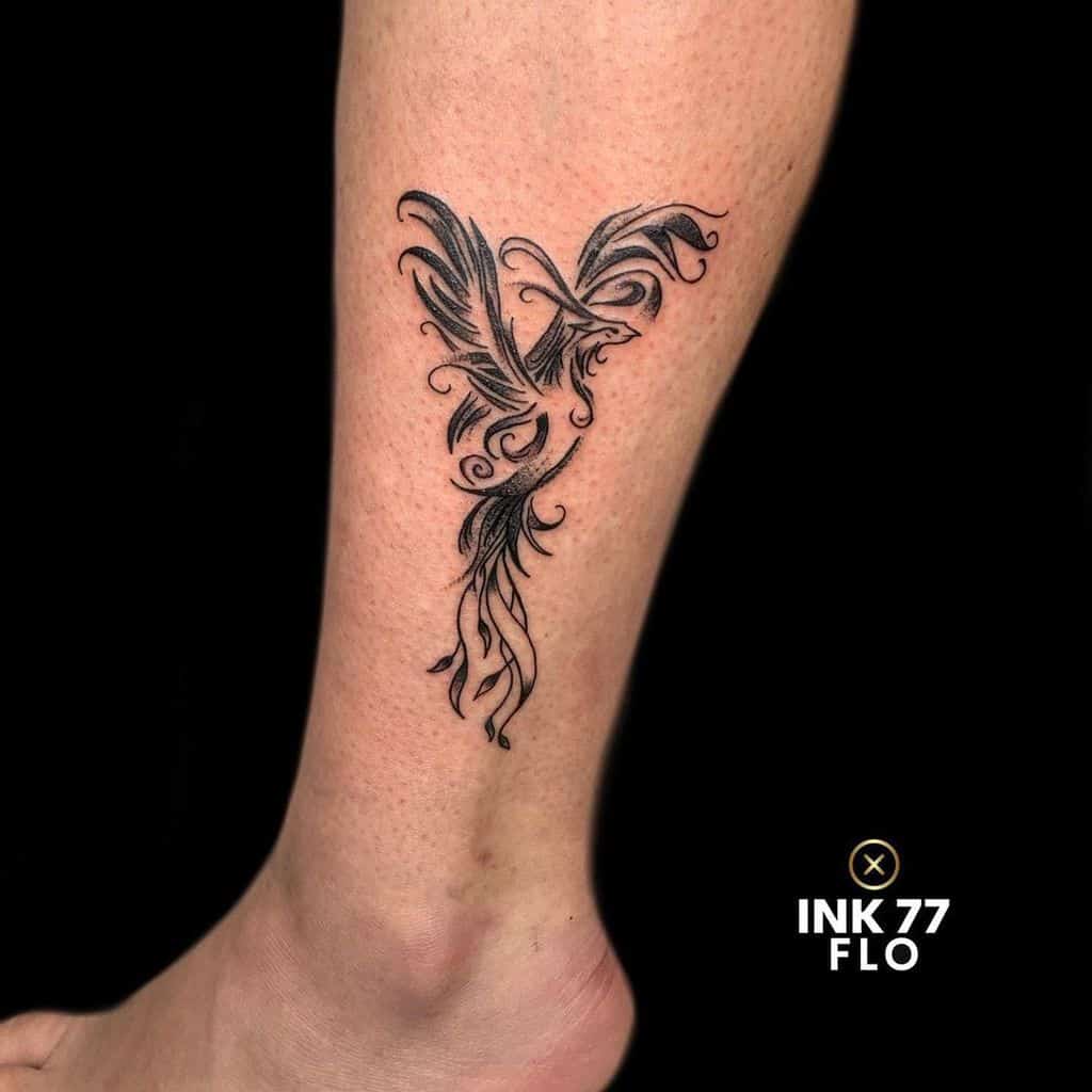 Abstract small phoenix rising tattoo in black ink on the lower leg