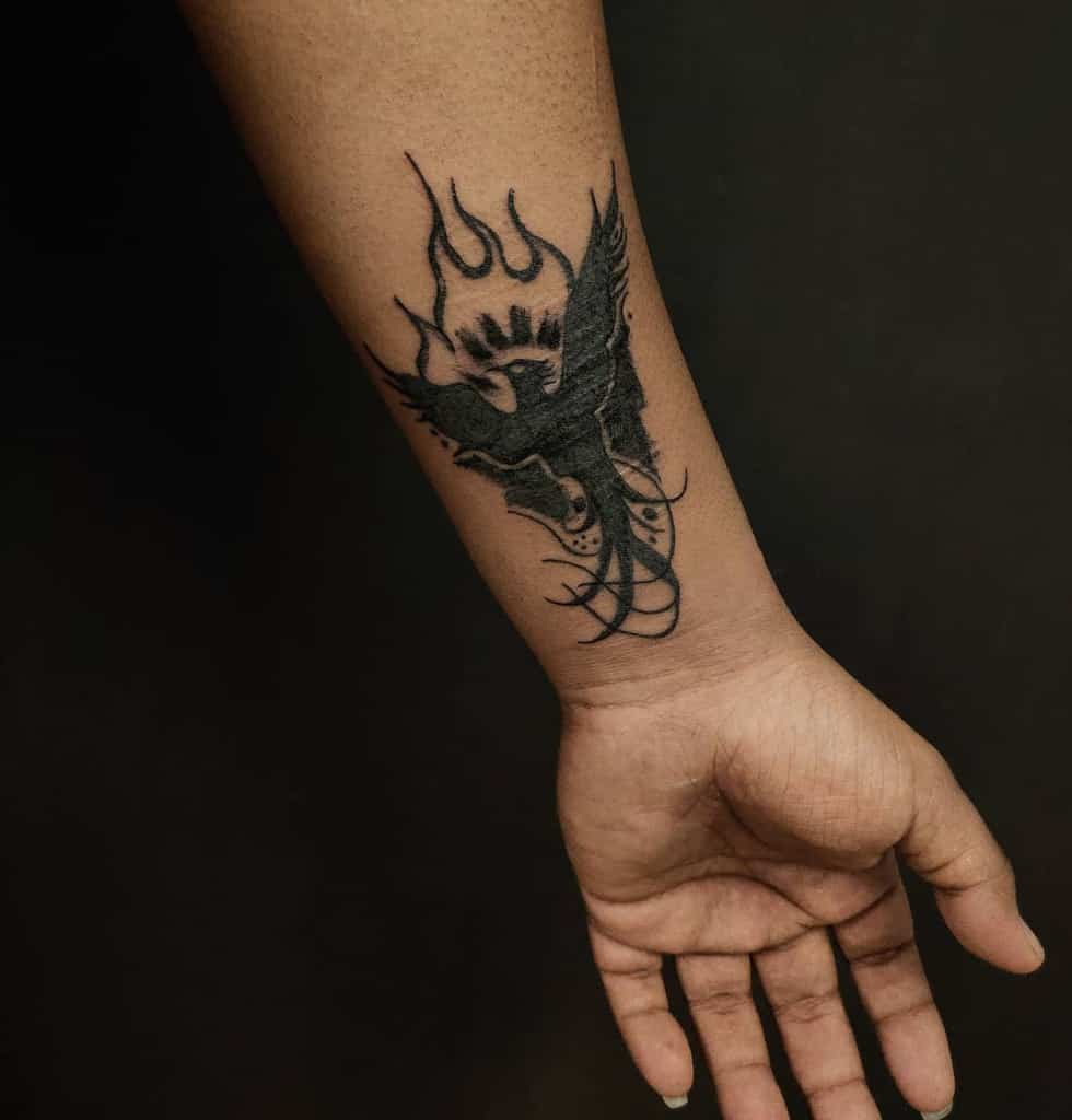 Forearm tattoo showcasing a small black phoenix rising from brilliant flames