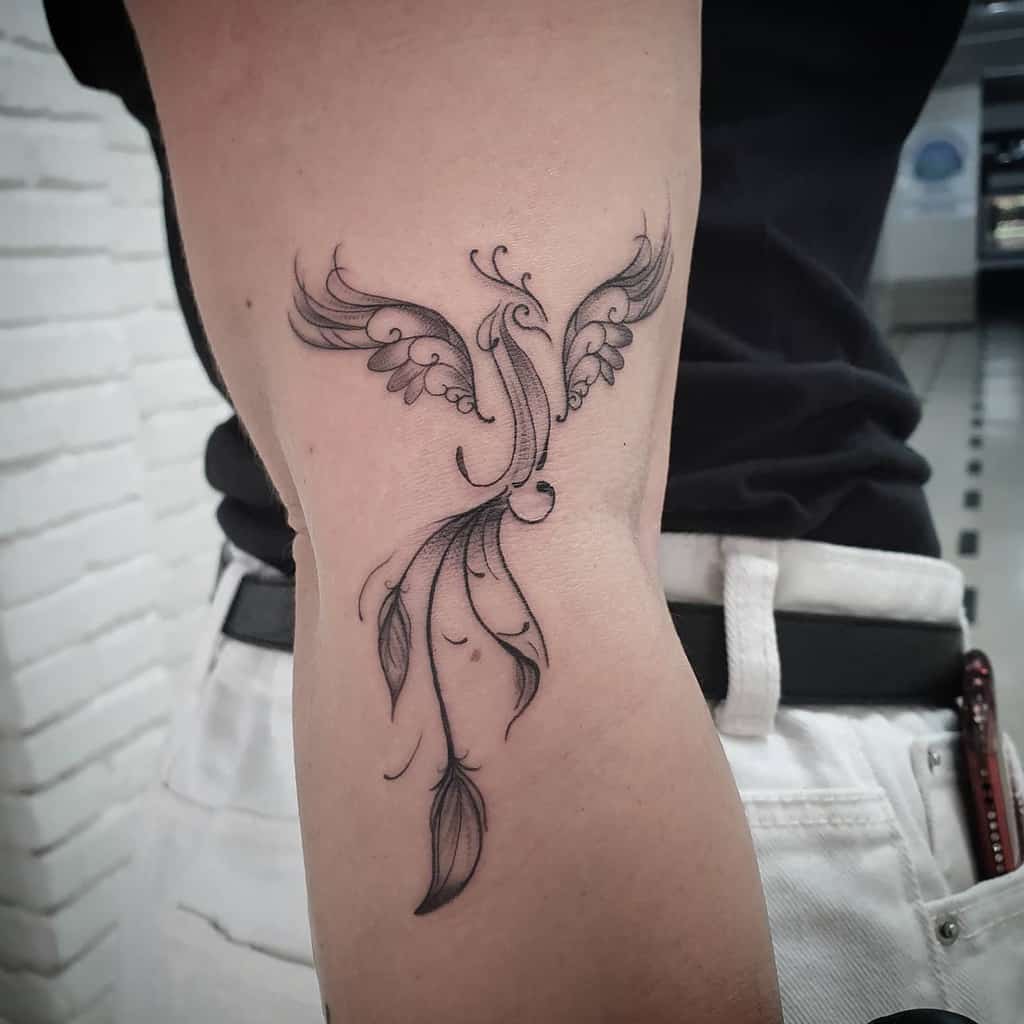 A black and white tattoo of a phoenix rising on a person's arm