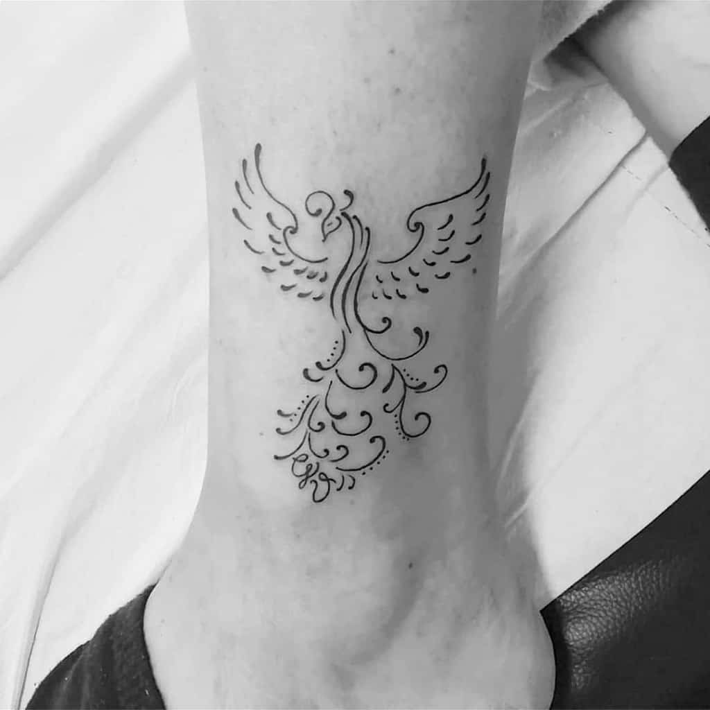 Line art tattoo of a stylized phoenix rising, elegantly located on an ankle