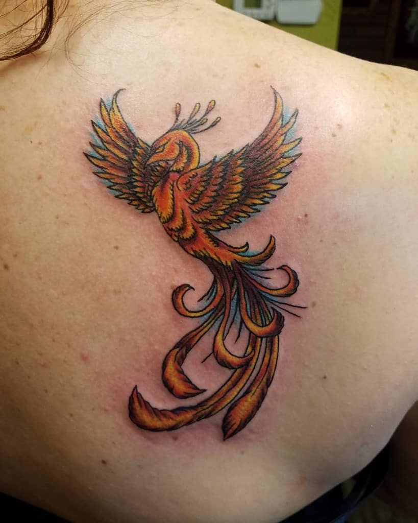 A vibrant phoenix tattoo on the shoulder, featuring warm orange and yellow hues with detailed feathers and flowing tail feathers
