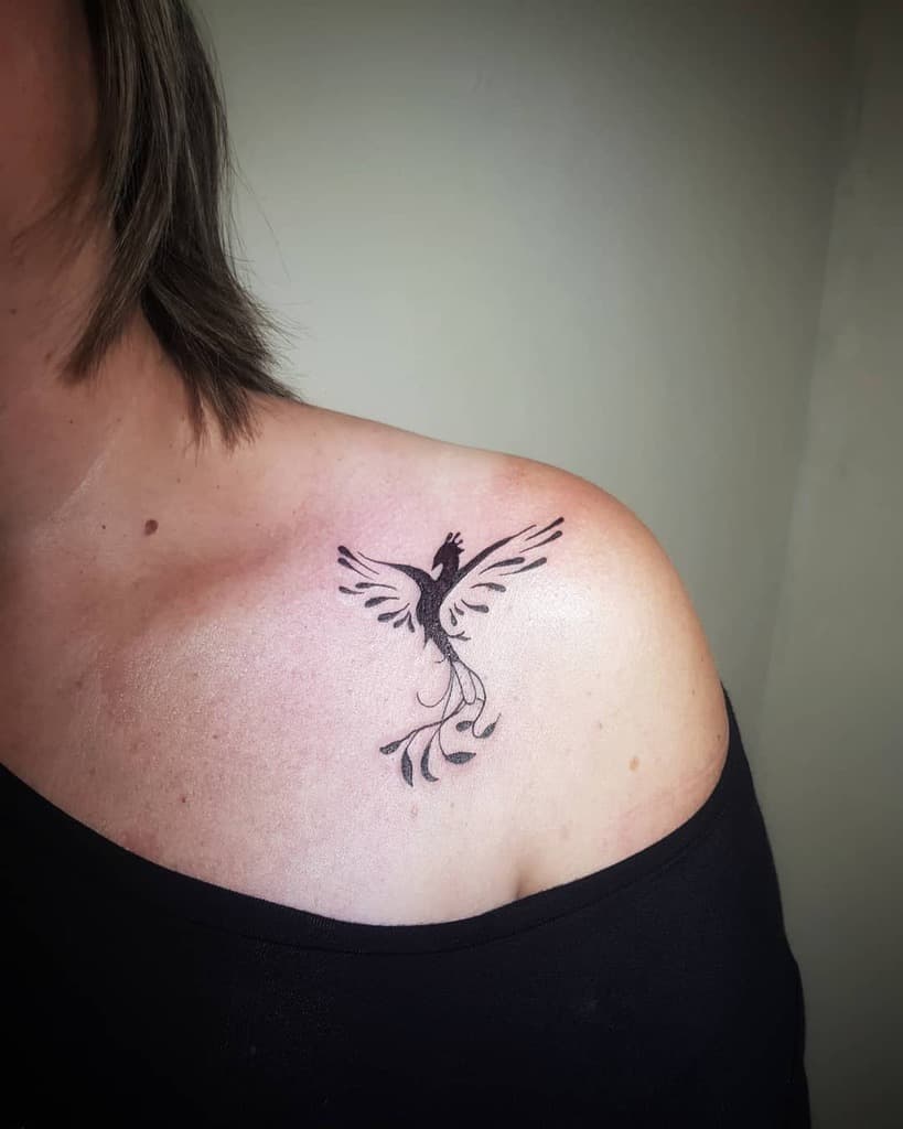 A small tattoo depicting a stylized phoenix gracefully rises from the woman's shoulder, capturing its mythical essence with intricate detail
