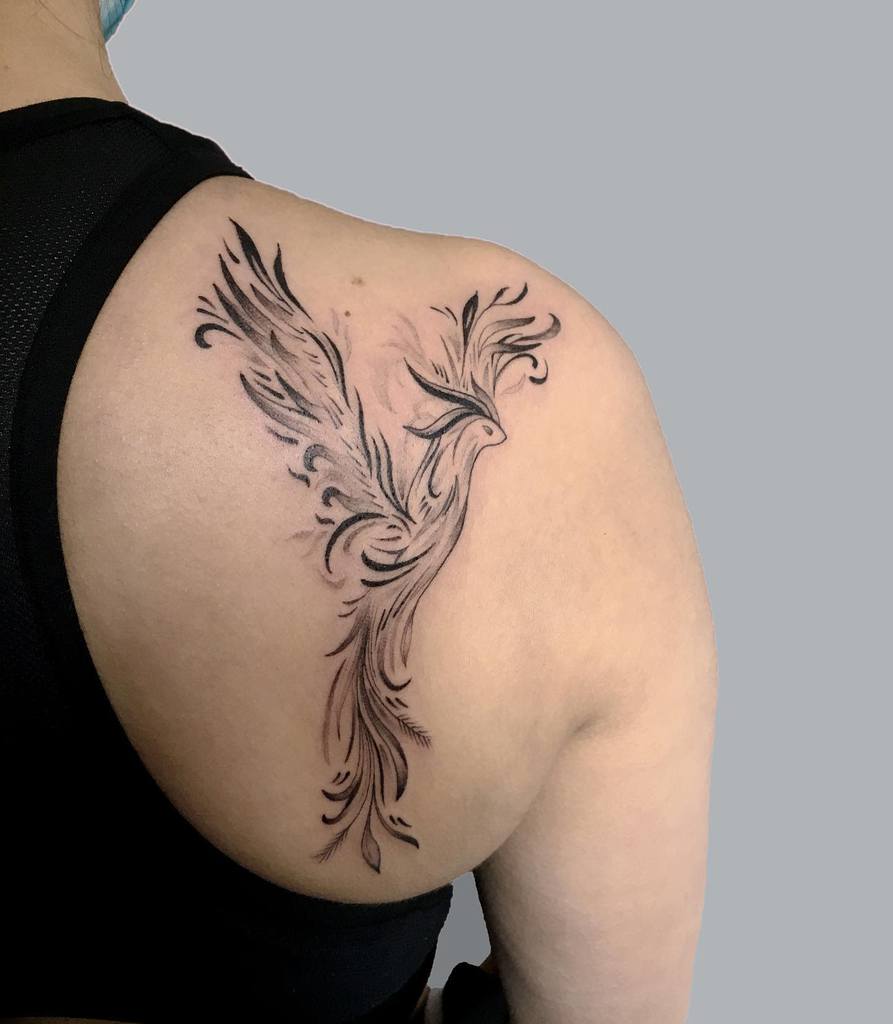 A stylized phoenix tattoo gracefully adorned a person's upper back and shoulder
