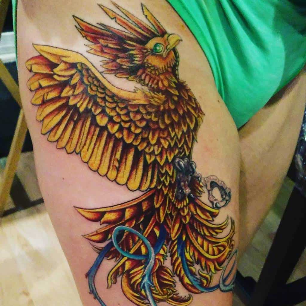 A colorful phoenix tattoo with outstretched wings on a thigh