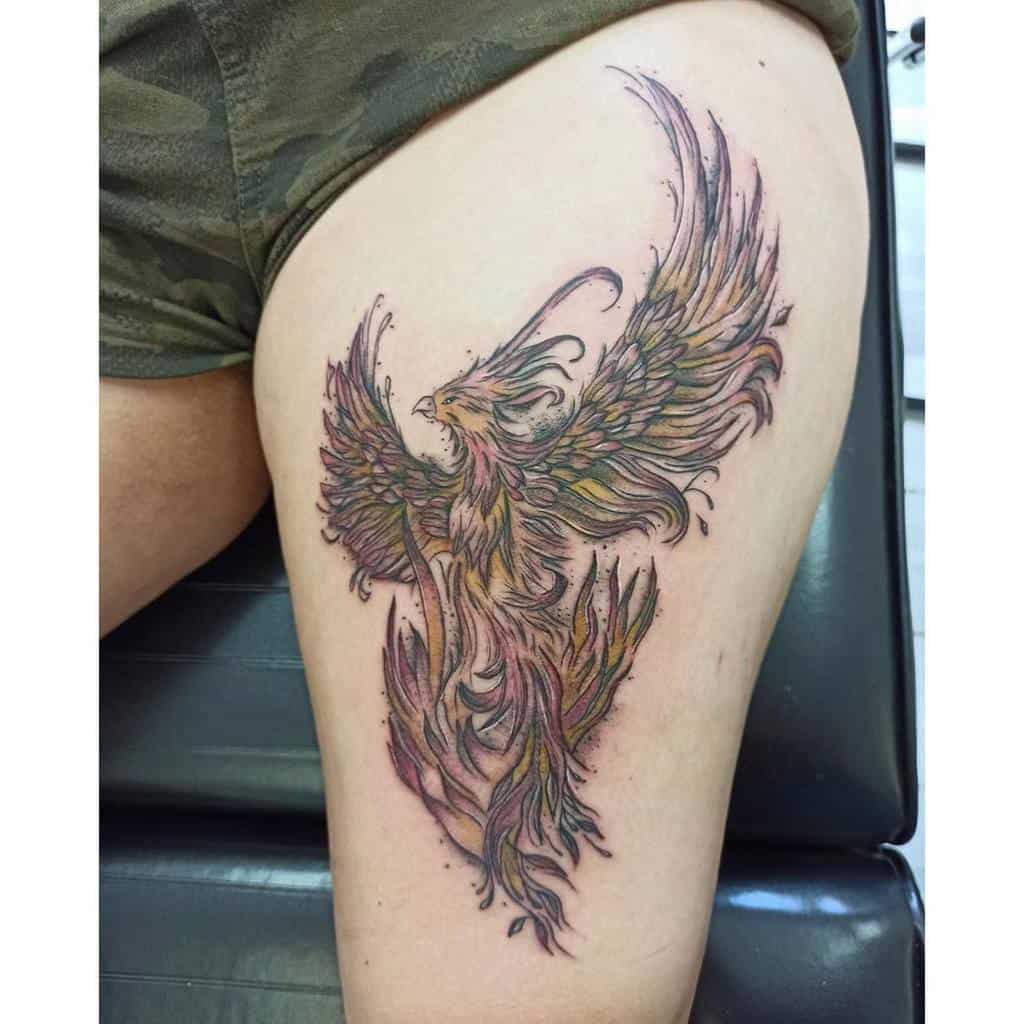 A colorful phoenix tattoo on the thigh, with vibrant shades of red, yellow, and purple, and detailed flowing feathers