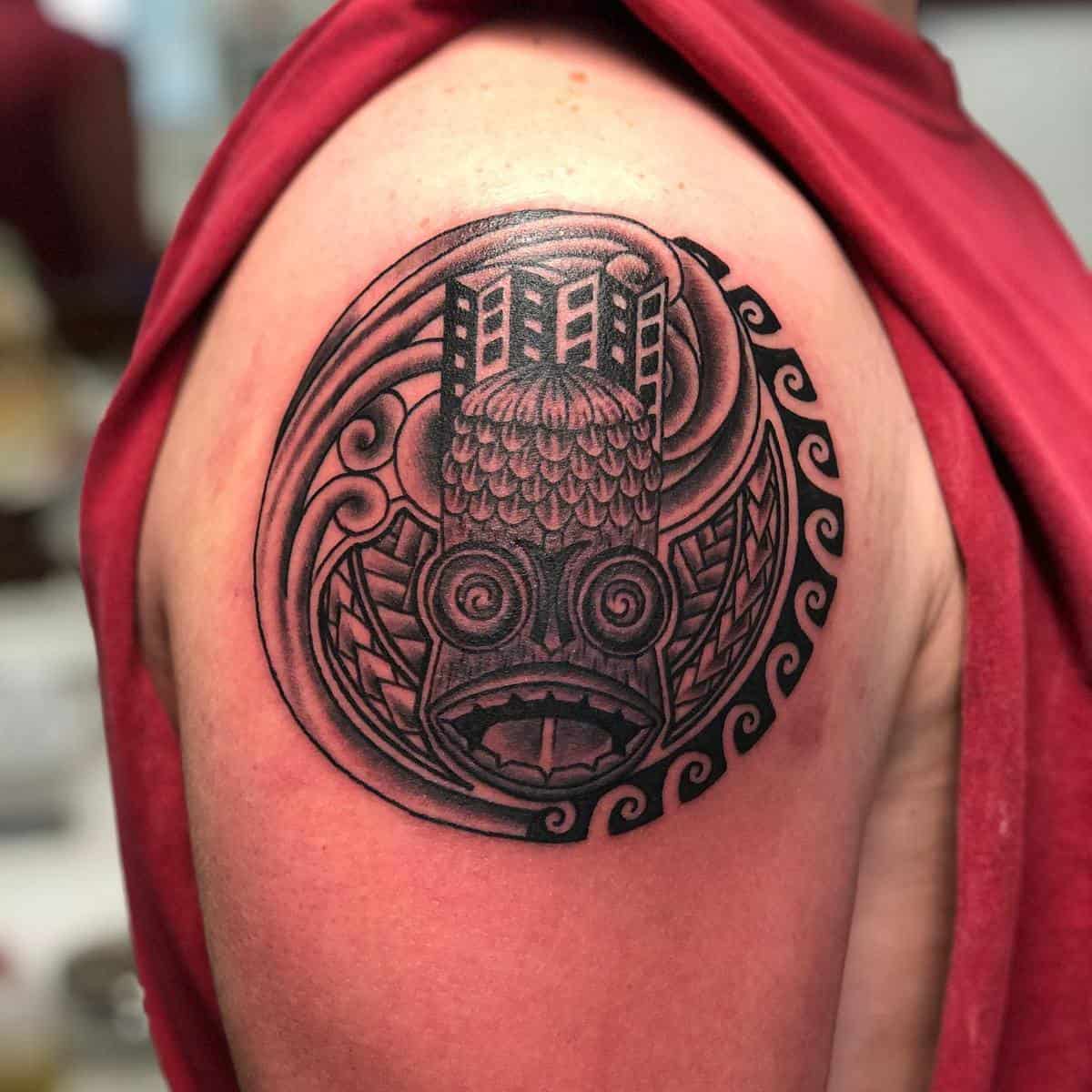 A tattoo on an upper arm featuring an intricate tribal design with geometric patterns and abstract elements