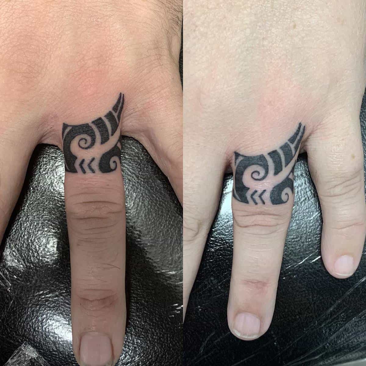 Close-up of a finger tattoo featuring black intricate, symmetrical tribal-style patterns on the ring fingers of both hands