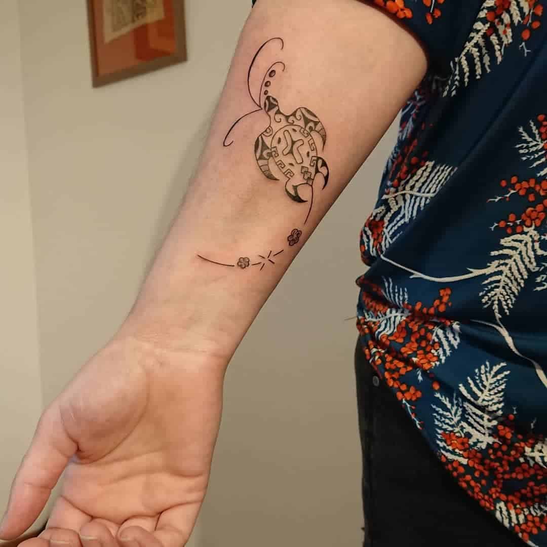 Forearm tattoo of a turtle with geometric shapes, dark shirt with red and white floral designs
