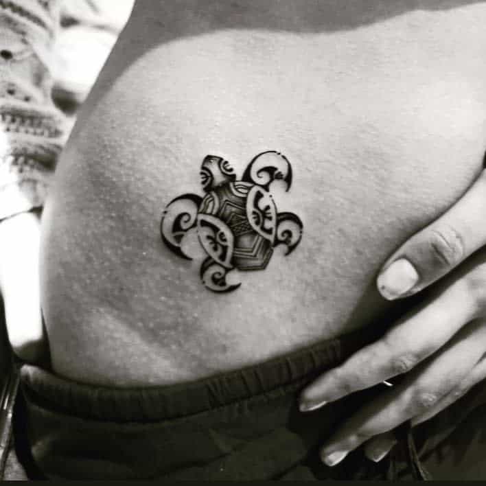 Black and white image of a detailed turtle tattoo on someone's skin, with a hand resting nearby