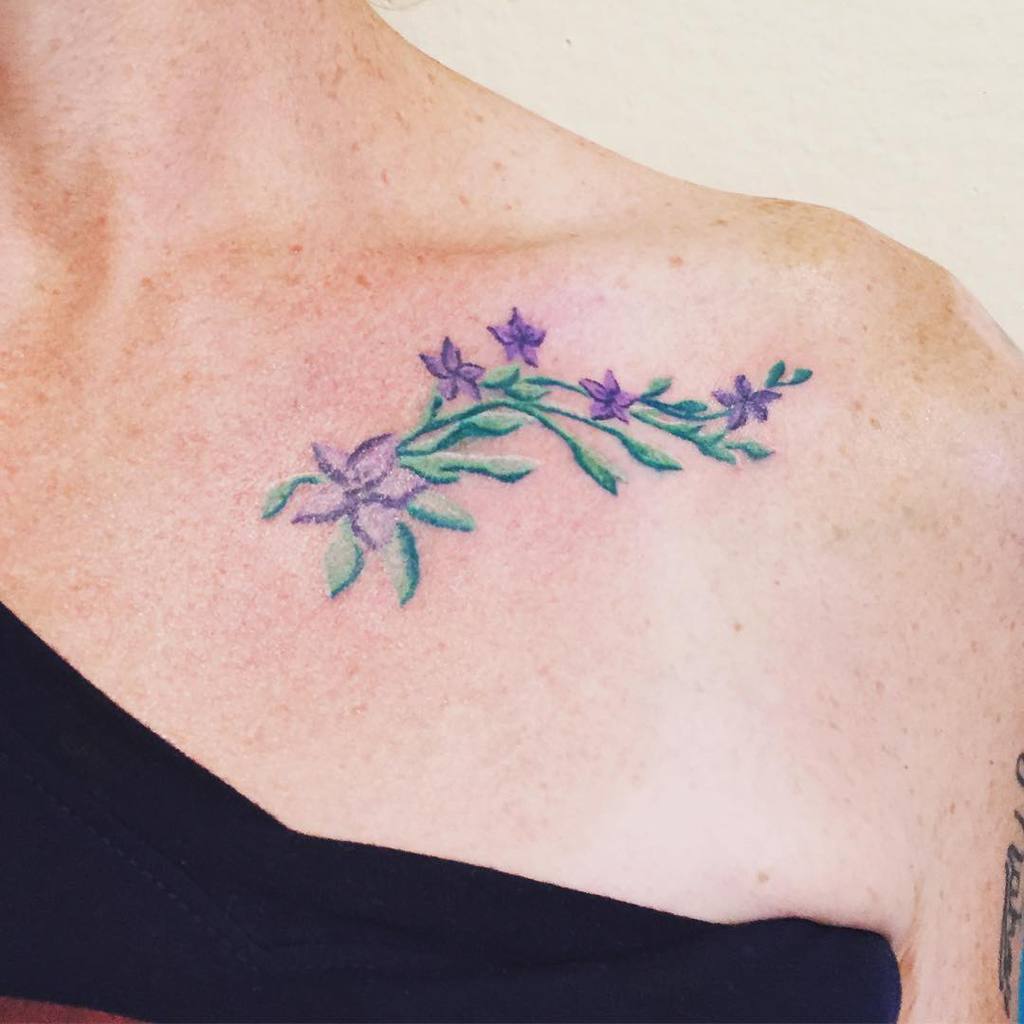 Floral tattoo with purple flowers and green leaves on a shoulder