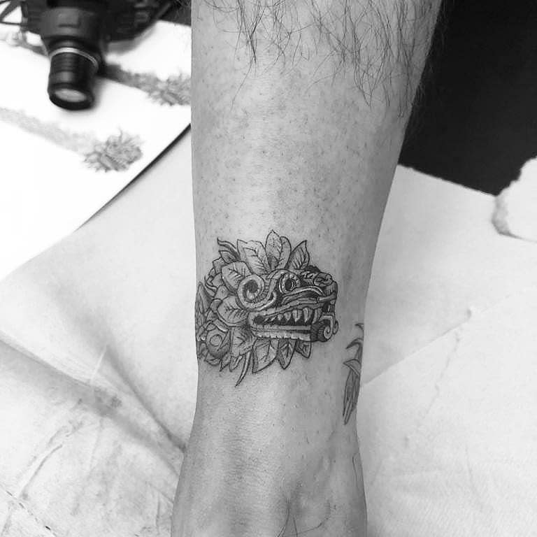 Small forearm tattoo of Quetzalcoatl's head with intricate linework and feather details