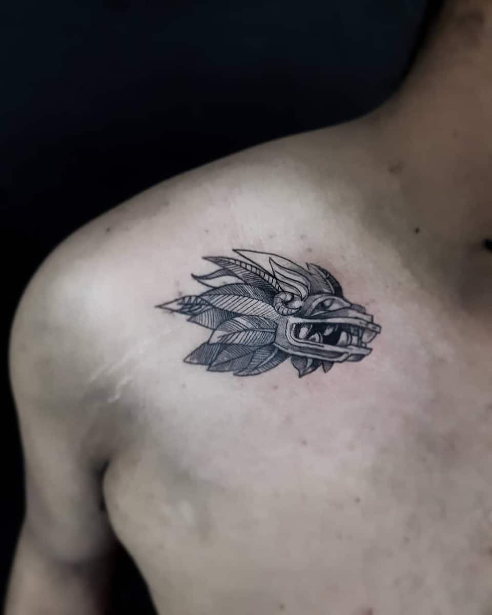 Detailed chest tattoo of Quetzalcoatl's head with intricate feathers and linework