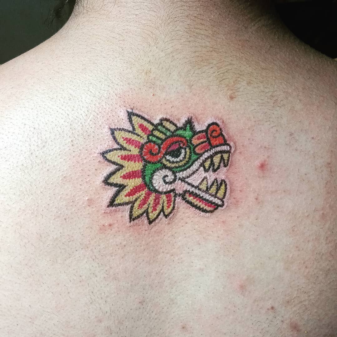 Colorful back tattoo of Quetzalcoatl's head with vibrant Aztec-inspired patterns