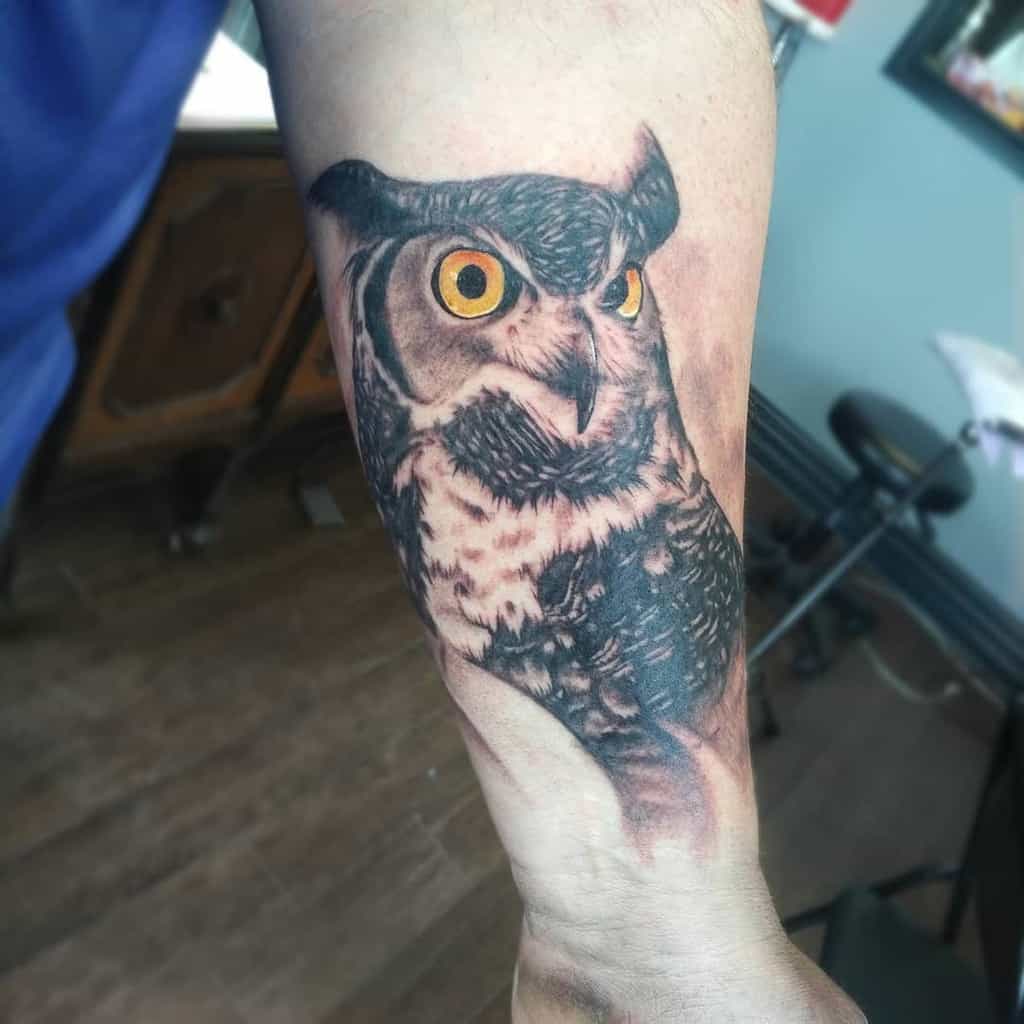 Forearm tattoo of a majestic owl with bright orange eyes and intricate feather detailing, capturing the essence of this wise creature