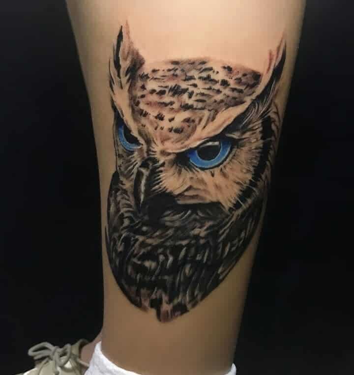 A striking tattoo features a detailed owl, its piercing blue eyes capturing attention on the wearer’s skin
