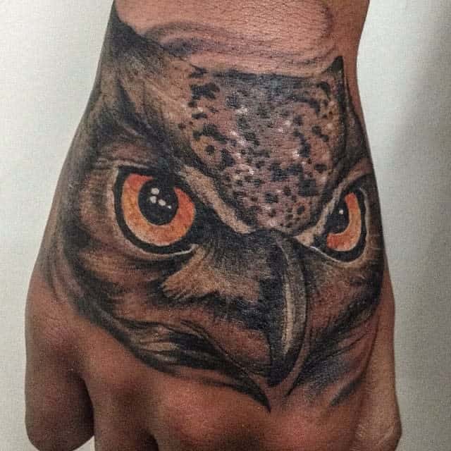 An intricate owl tattoo graces the back of the hand, showcasing detailed eyes and meticulously crafted feathers