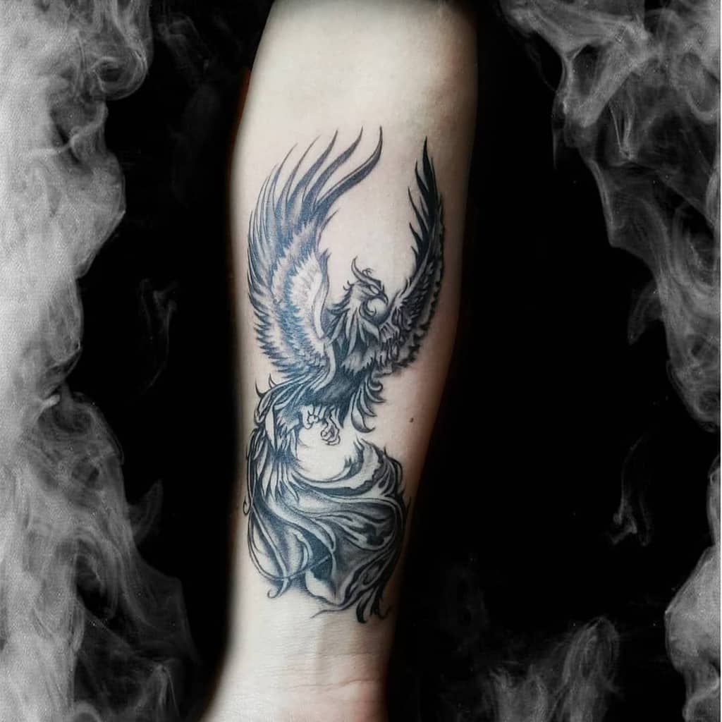 A stunning black and grey phoenix tattoo graces the forearm