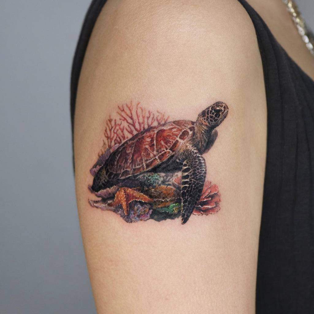 A vibrant, realistic tattoo of a turtle resting on coral and surrounded by colorful ocean elements, placed on the upper arm