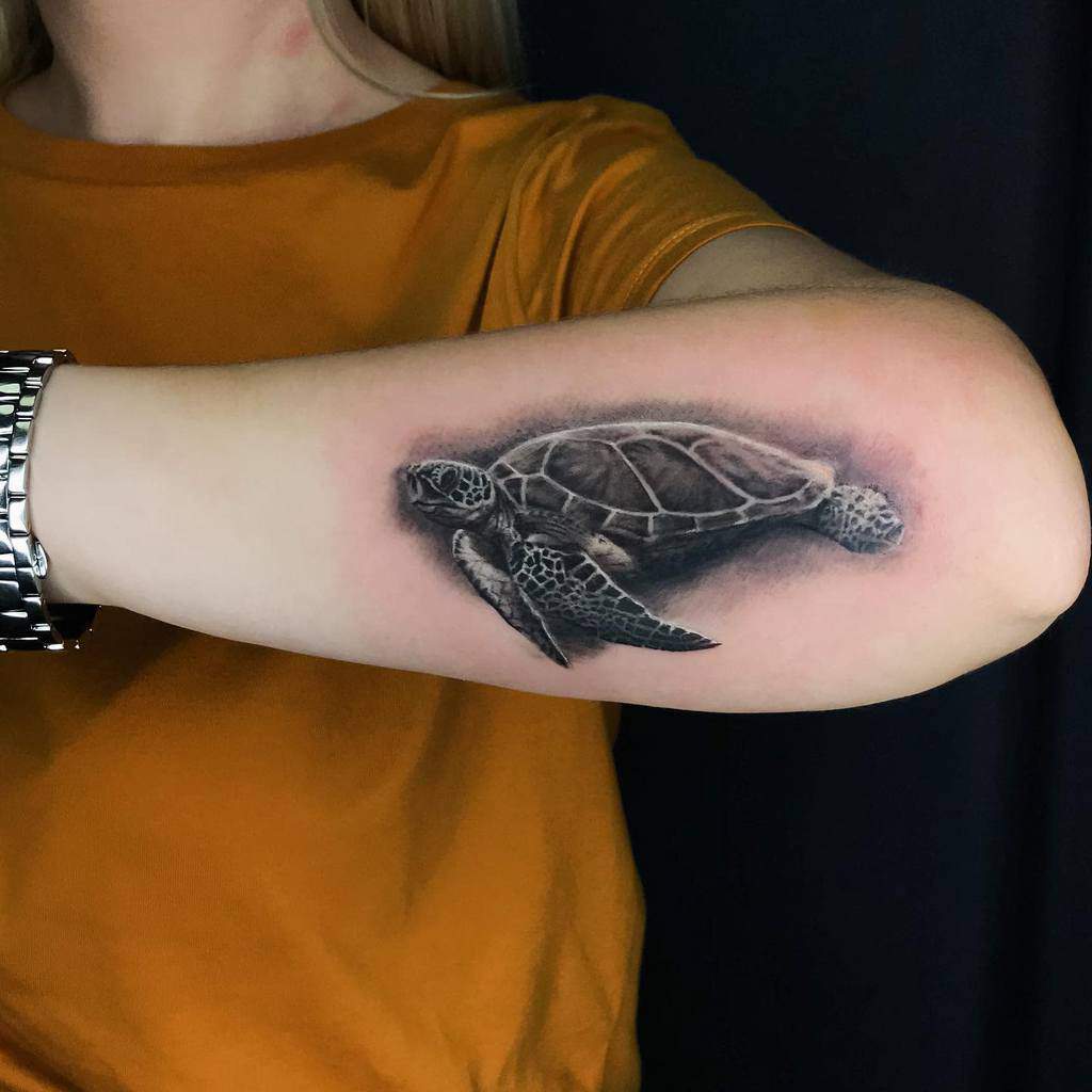 A realistic black and grey tattoo of a swimming turtle on the forearm, showcasing detailed shading and texture