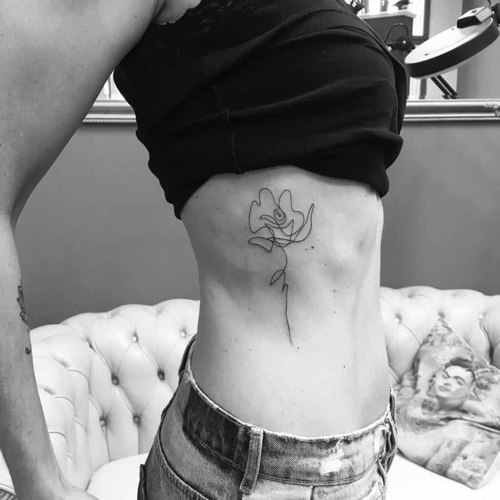 A woman is showcasing a minimalist rose tattoo on her ribcage 
