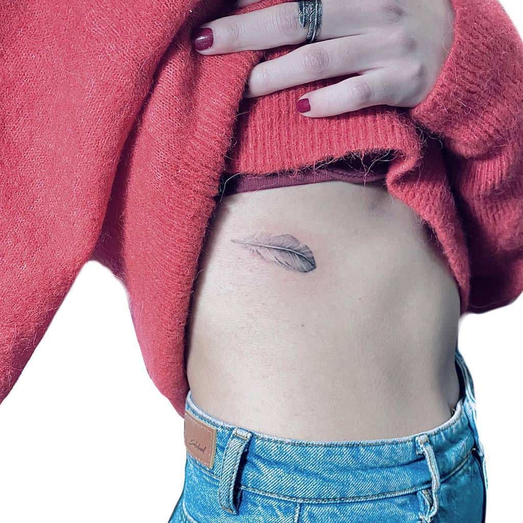 Fine-line feather tattoo on the ribcage, symbolizing lightness and freedom, with soft shading for a delicate and elegant look