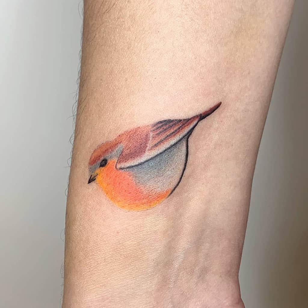Small and colorful tattoo of a robin in flight, with soft shading and bright colors on the robin's chest and wings, captured in a dynamic pose