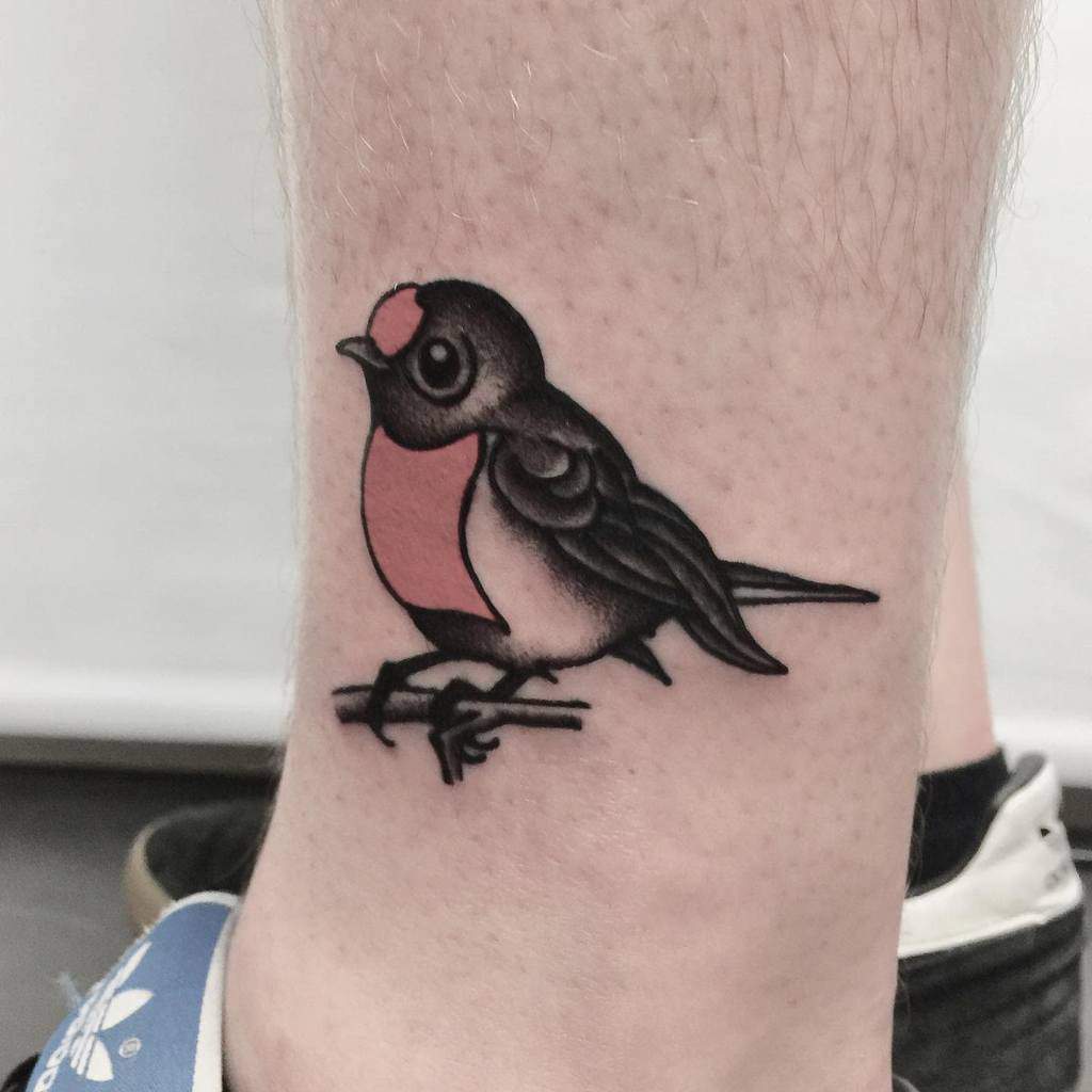 A tattoo of a small robin with black wings and a pink belly perched on a branch
