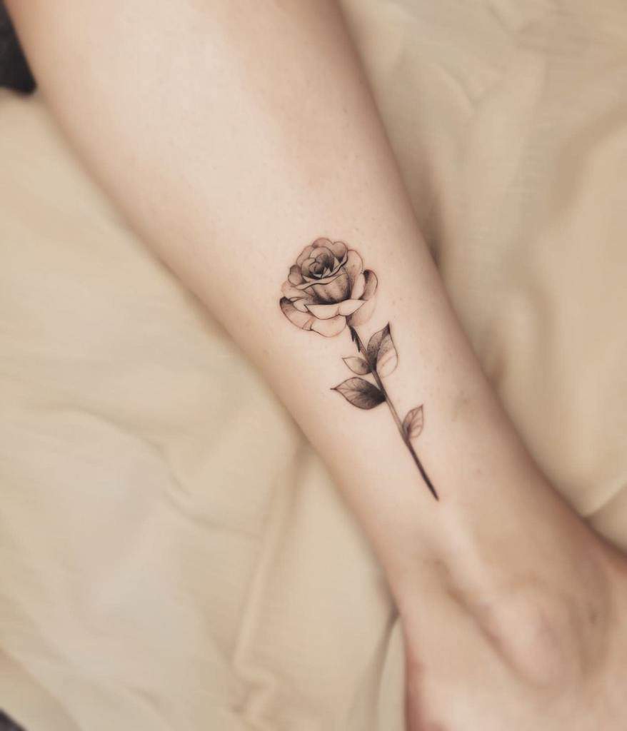A black and gray rose tattoo on an ankle