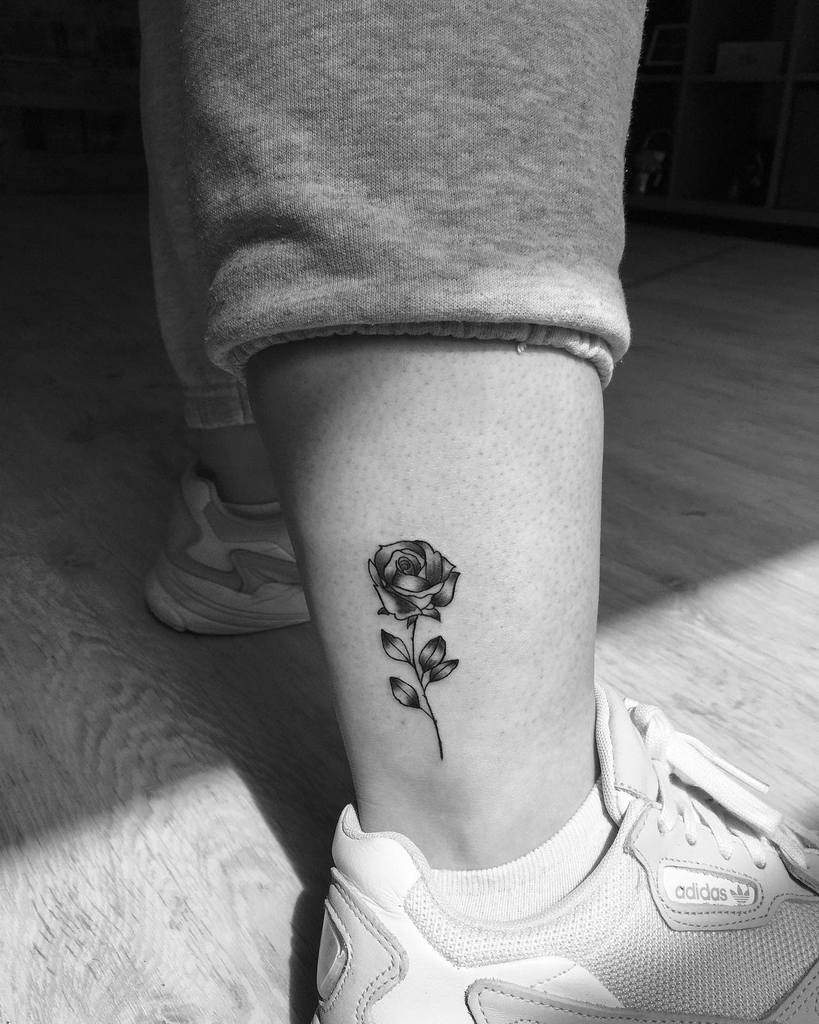Black and white tattoo of a rose on a person's ankle