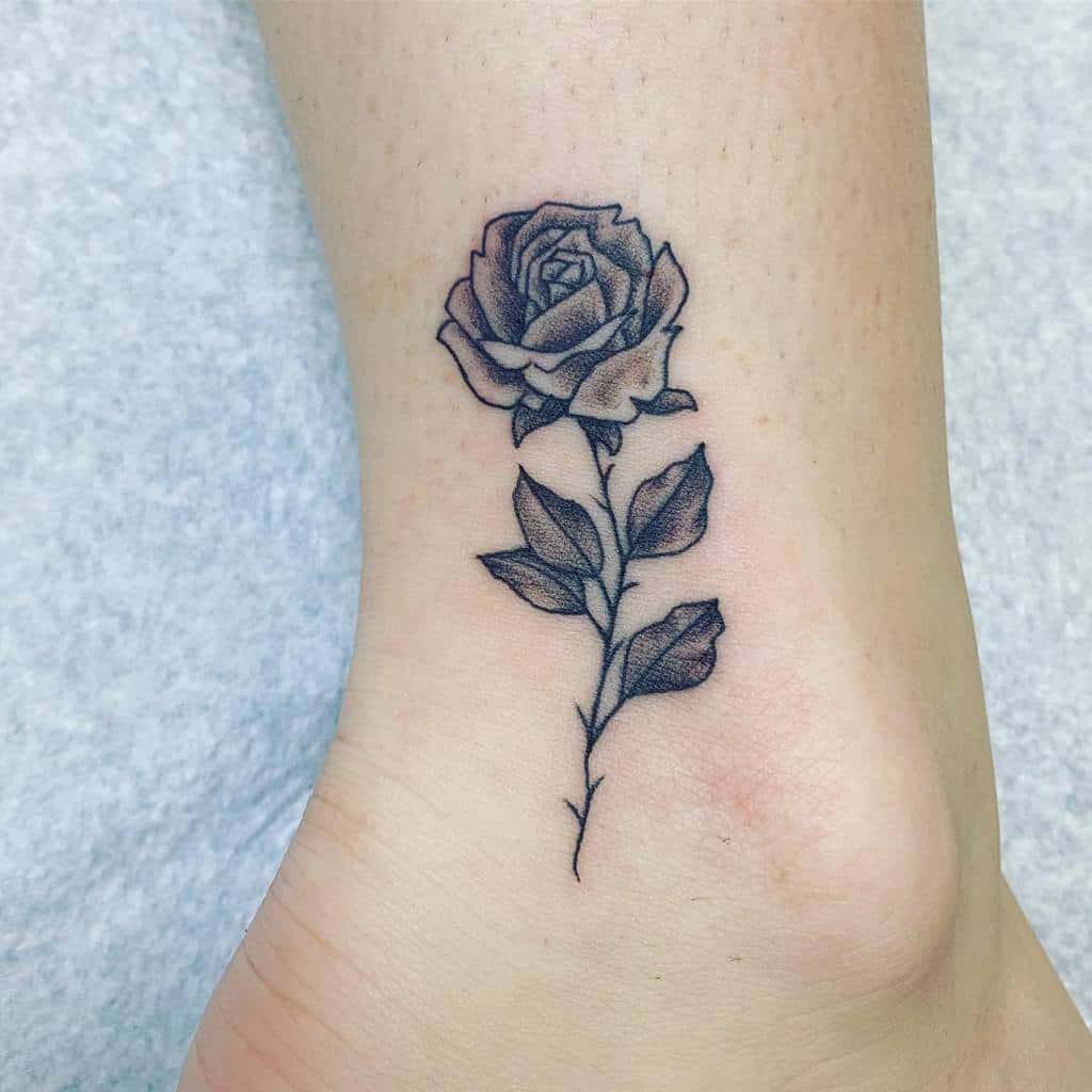 A black rose tattoo with leaves on an ankle