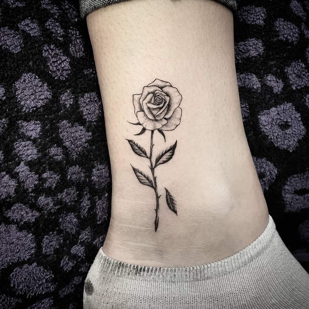 Black and grey rose tattoo on the ankle, featuring fine-line details and soft shading for a realistic look