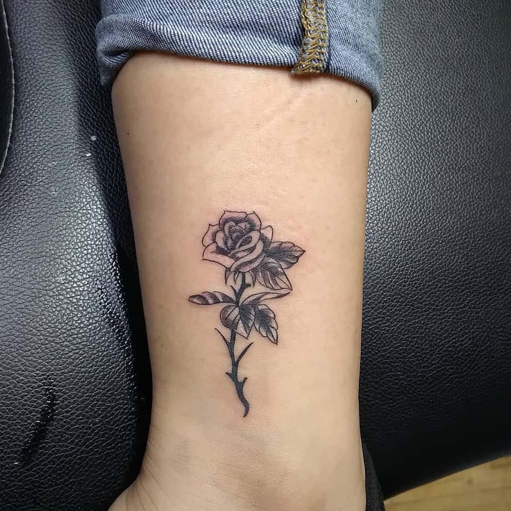Black and grey rose tattoo on the ankle, featuring intricate shading and fine details for a realistic floral design