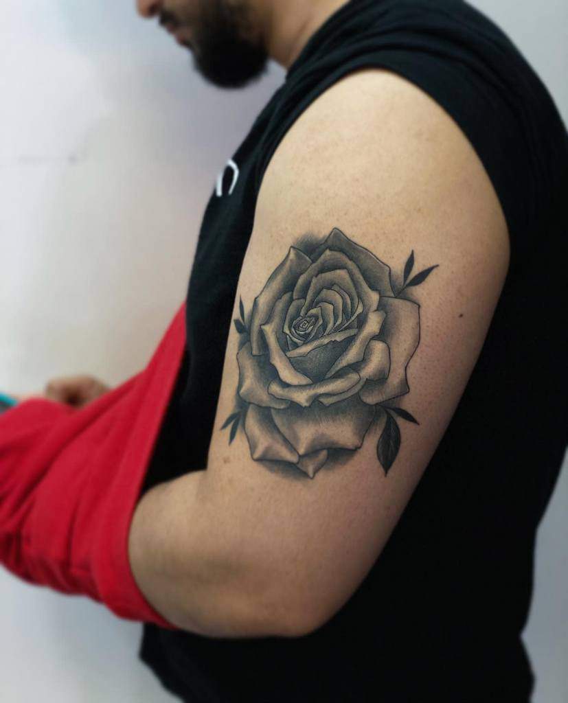A man with a black and gray rose tattoo on his upper arm