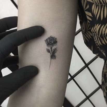 A small black rose tattoo on a forearm