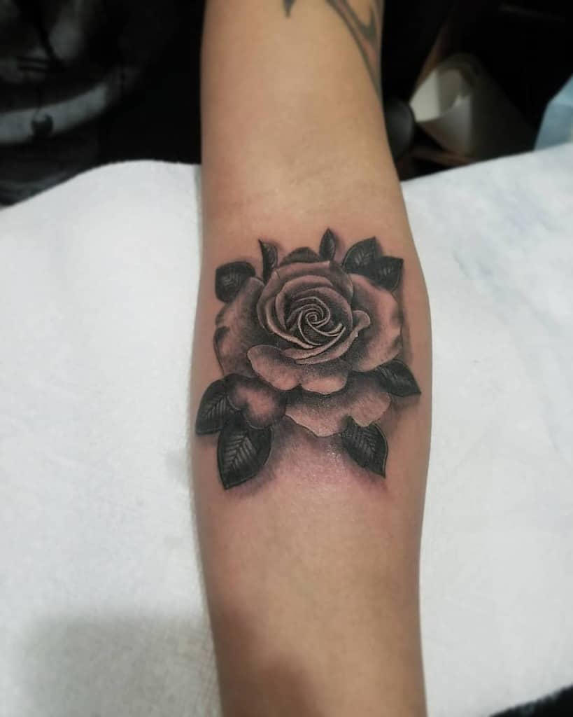 Close-up of a black and gray rose tattoo on a forearm