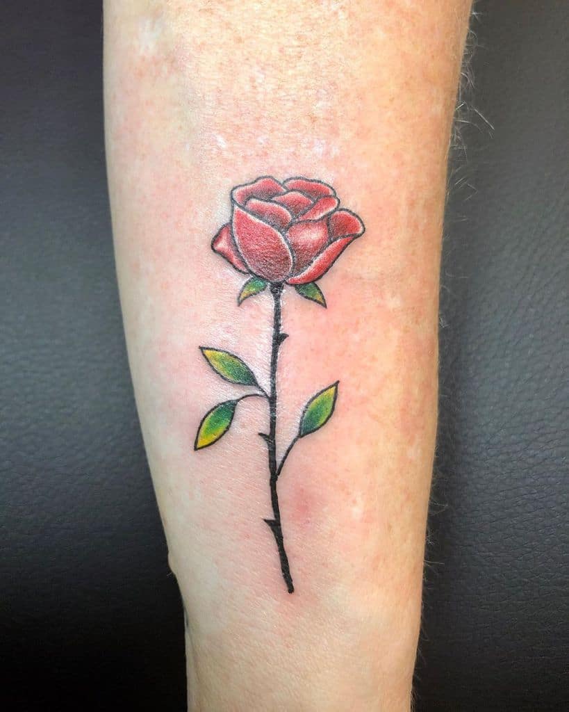 A realistic red rose tattoo with green leaves on a forearm