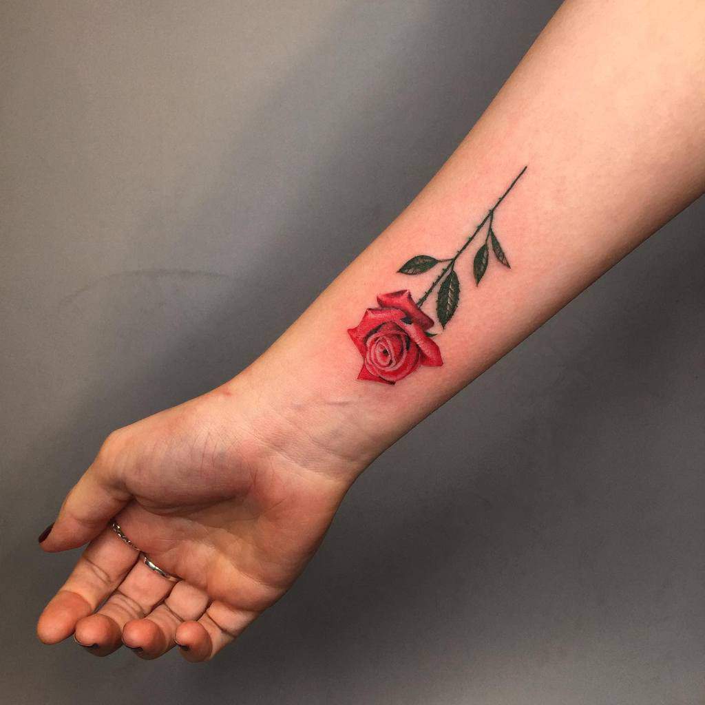 A red rose tattoo on a forearm with a green stem and leaves