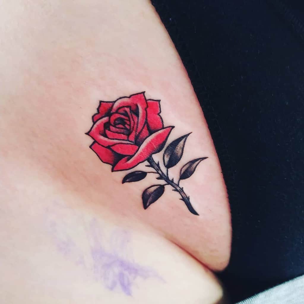Close-up of a red rose tattoo on skin, with black leaves and stem