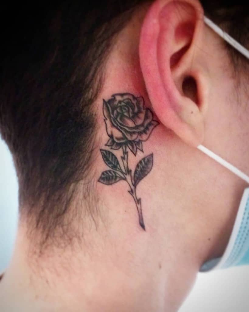 Black and grey rose tattoo behind the ear, featuring fine-line details and soft shading for a bold yet elegant look