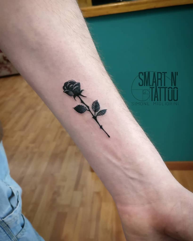 Black rose tattoo on a person's inner forearm