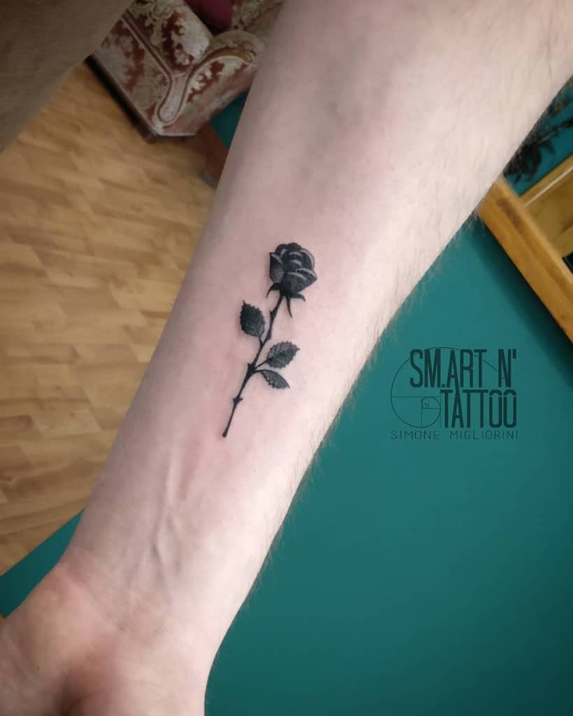 Black rose tattoo on inner forearm