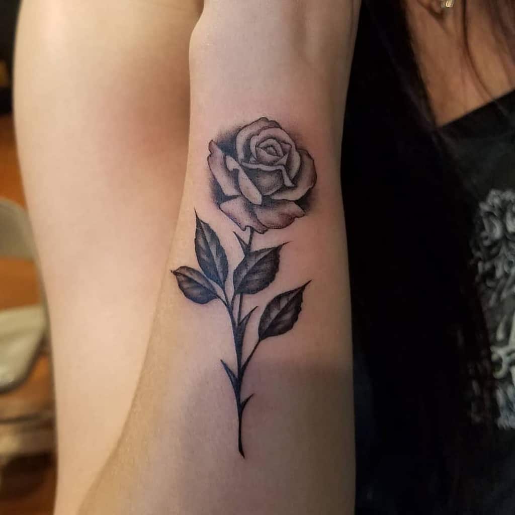 Tattoo of a detailed black rose with leaves on a forearm