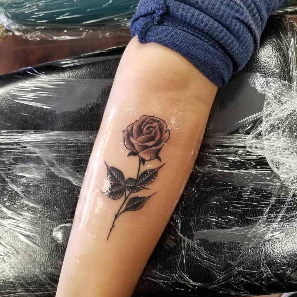 Tattoo of a realistic rose with leaves on a forearm
