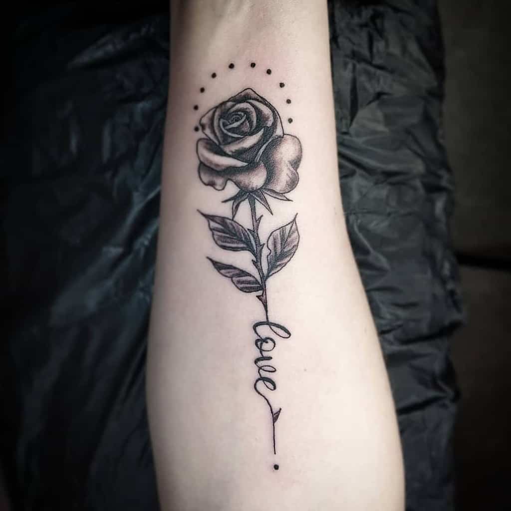Tattoo of a rose with dots above and the word "love" below on a forearm