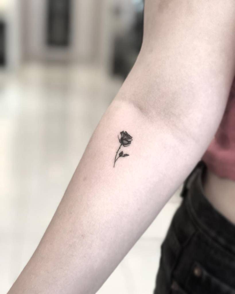 A small, delicate rose tattoo on a person's inner forearm