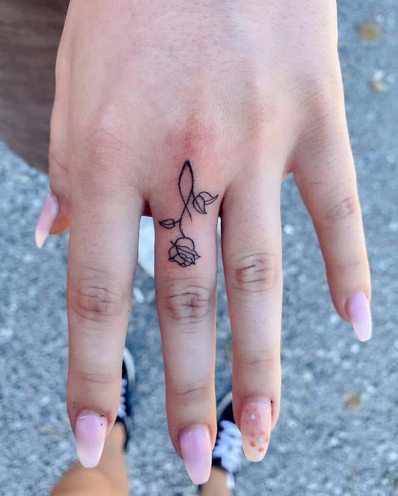 Hand with a delicate rose tattoo on the middle finger